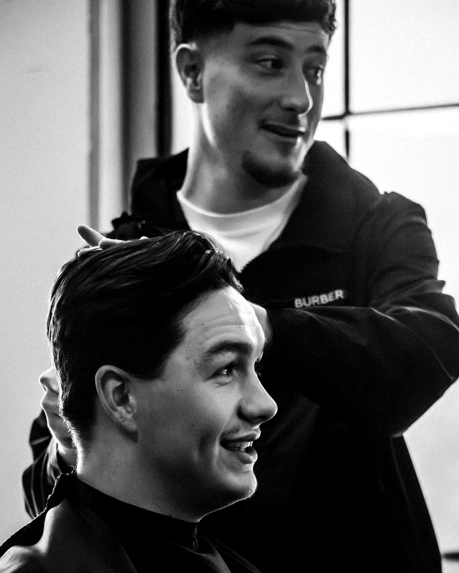 A barber shares a joke with a client mid-cut, in black and white