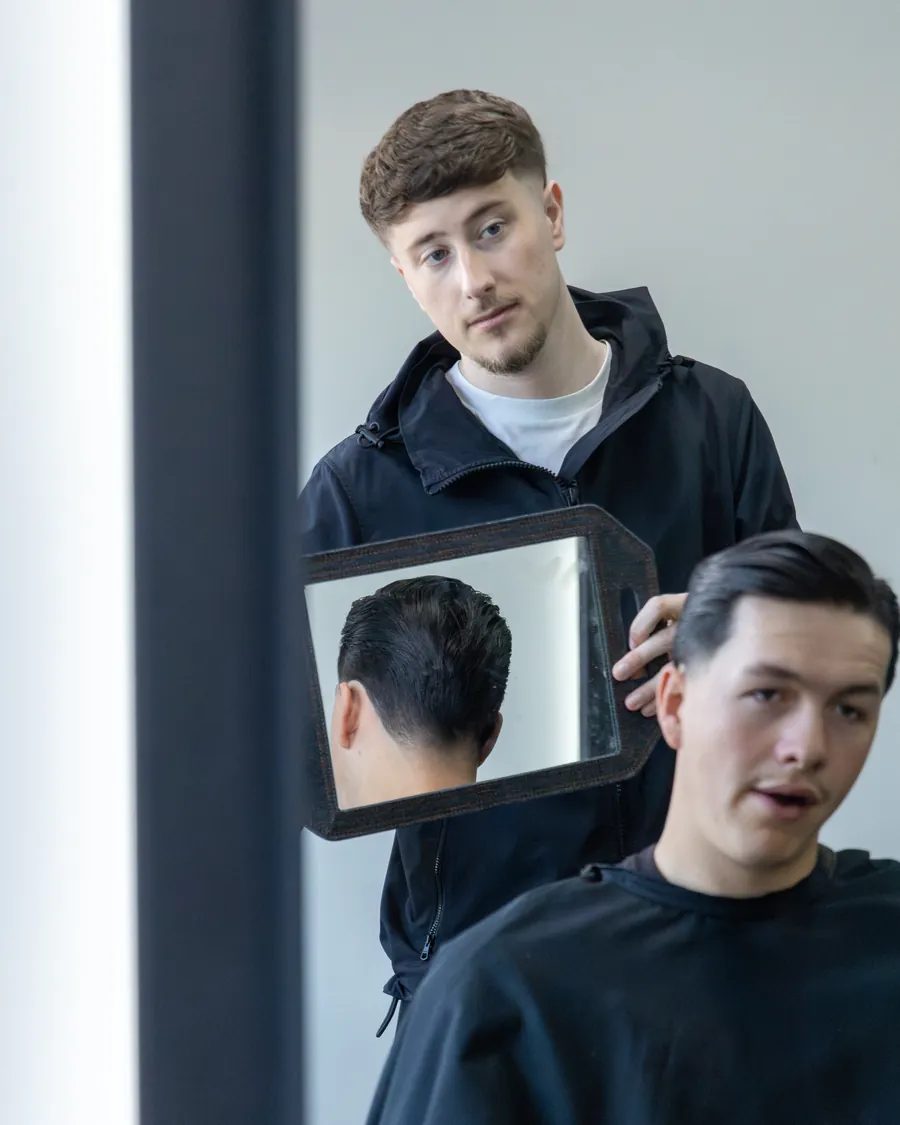 A barber holds up a hand mirror so the client can check the back of his cut